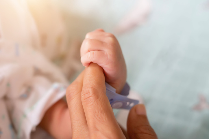 Photo shows an adult holding a newborn baby's hand/Getty Images