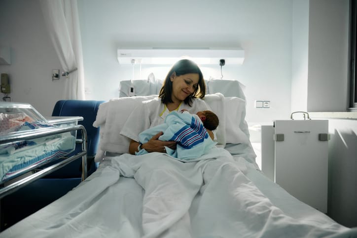Photo shows a mother holding her newborn in a hospital bed/Getty Images