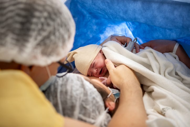 Photo shows two parents seeing their baby during a c-section delivery/Getty Images