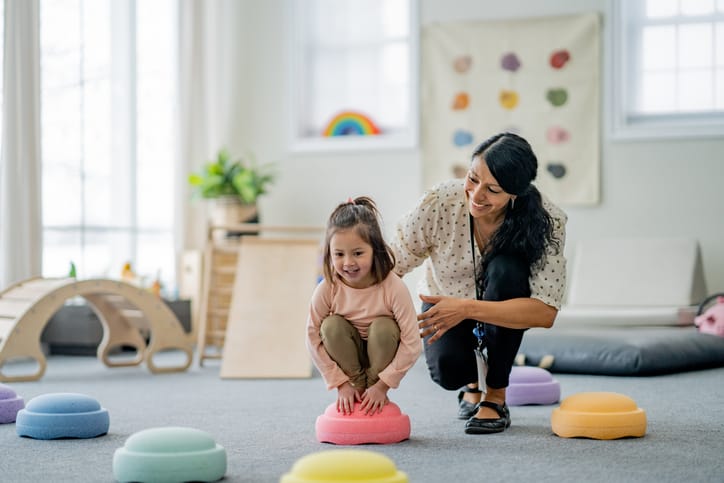 Photo shows a female physiotherapist working with a young girl on her balancing during a play therapy session/Getty Images