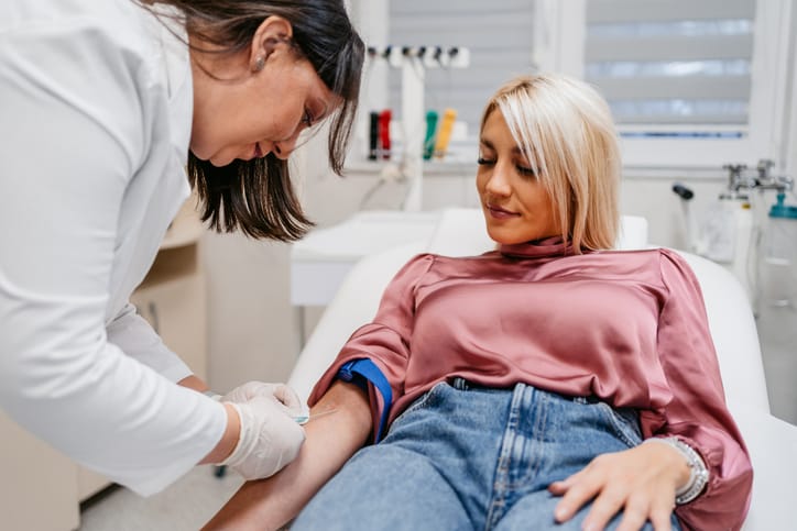 Photo shows a female doctor taking a blood sample from a female patient in a medical clinic/Getty Images