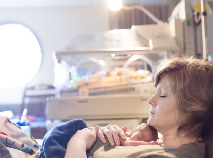 Photo shows a newborn baby sleeping soundly in the NICU with his mother/Getty Images