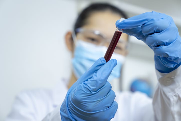 A scientist looks closely at a vial of blood/Getty Images