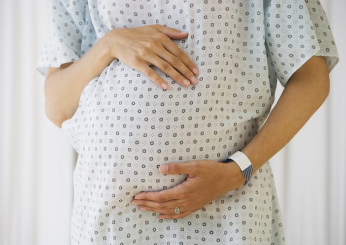 A pregnant woman in a hospital gown holds her stomach/Getty Images