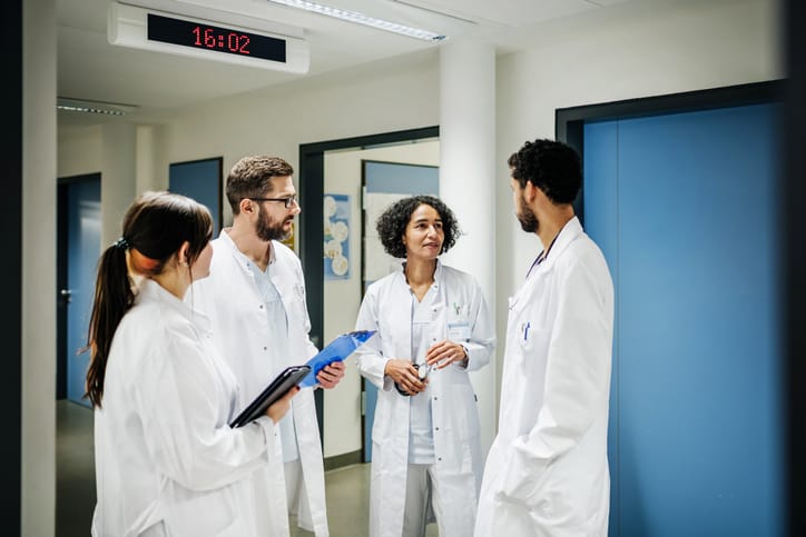 Photo shows a group of clinical doctors with charts chatting at the hospital/Getty Images