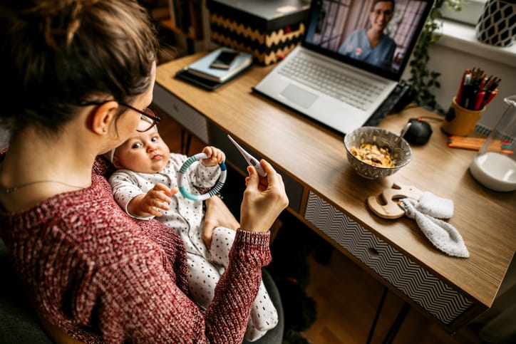 Photo shows a mother holding her baby during a telemedicine appointment/Getty Images