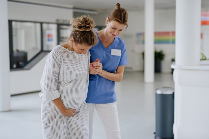 Photo shows a nurse helping a pregnant woman with painful labor contractions in the hospital hall/Getty Images