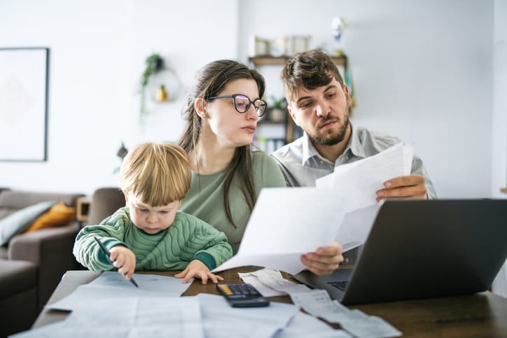 Photo shows parents and their toddler sitting at a table and looking at bills/Getty Images