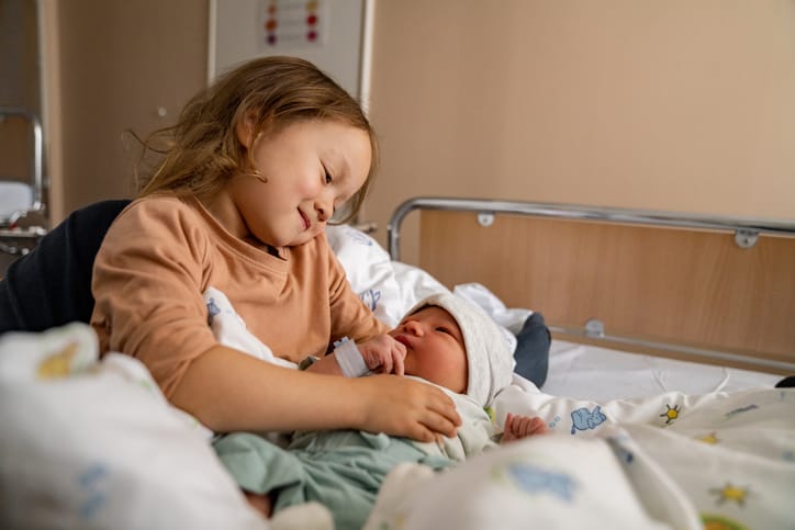 Photo shows a young child sitting next to her newborn brother in a hospital room/Getty Images
