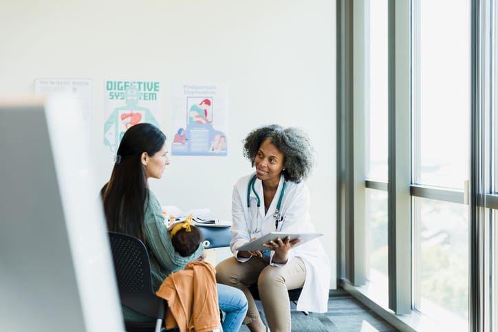 Photo shows a mother holding her baby while speaking with a doctor/Getty Images