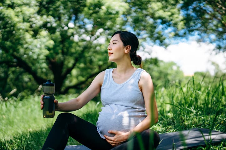 Photo shows a young pregnant woman taking a break from exercising outdoors/Getty Images