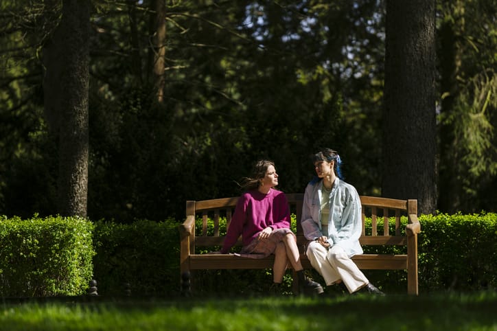 Photo shows two women sitting on a bench in the sunshine and chatting/Getty Images