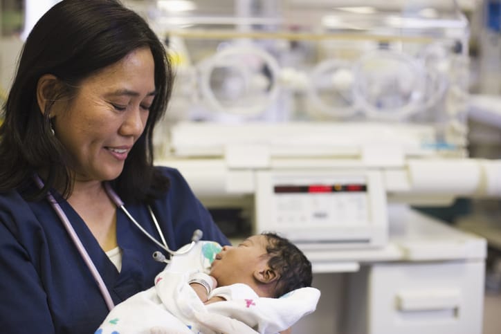 Photo shows a nurse holding a newborn in a hospital/Getty Images