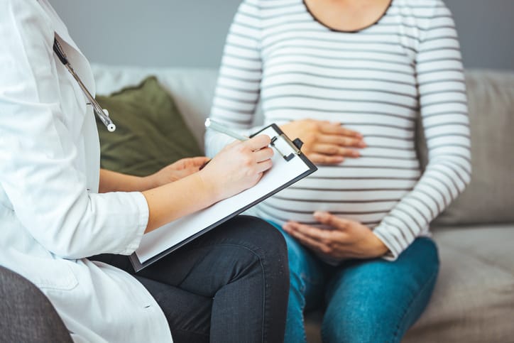 Photo shows a pregnant woman holding her stomach while a doctor writes on a clipboard/Getty Images