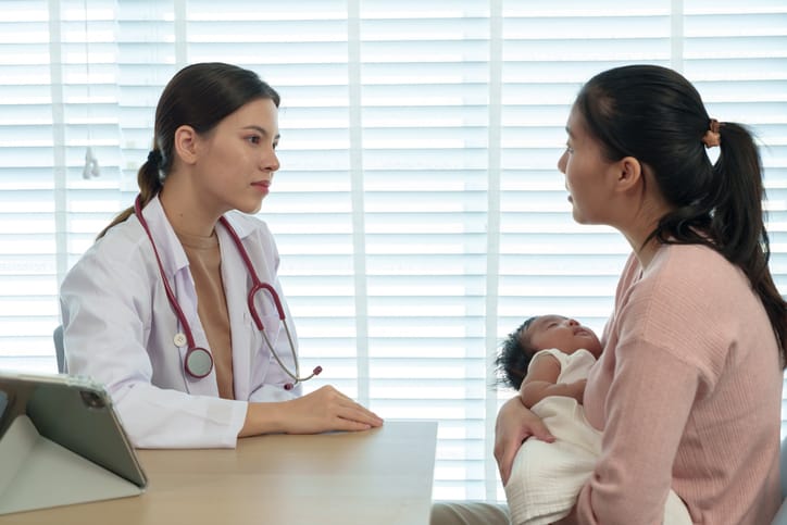 Photo shows a mother holding her newborn while speaking with a pediatrician/Getty Images