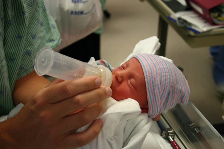 Photo shows the hands of a new father feeding his newborn preemie son the first drops of his mother's colostrum/Getty Images