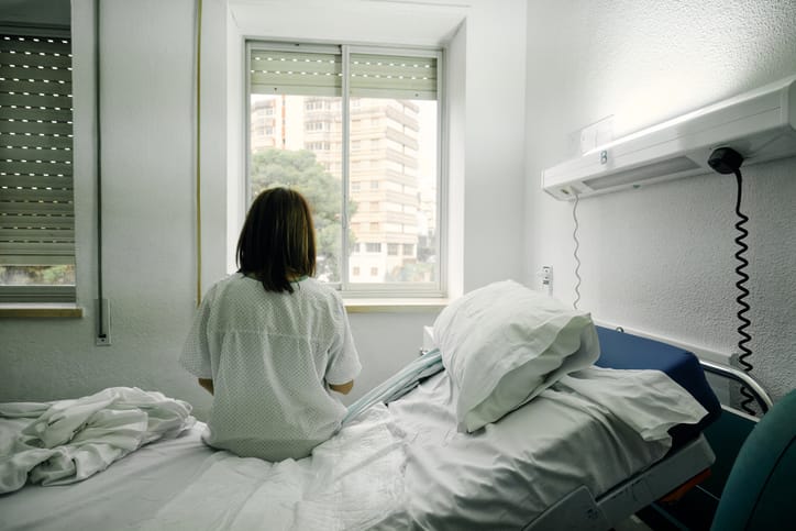Photo shows a woman sitting on the bed of a hospital room looking out the window/Getty Images