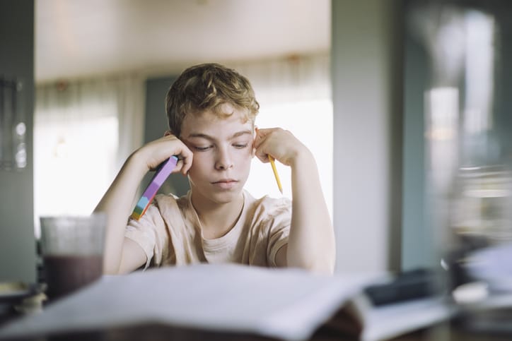 Photo shows a young boy holding a fidget toy while doing homework/Getty Images