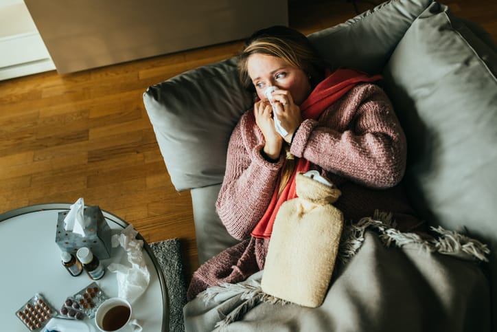 Photo shows a woman lying on the couch and blowing her nose/Getty Images
