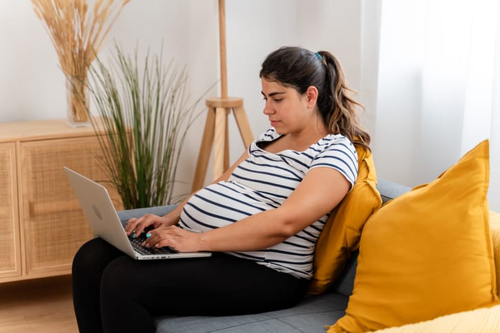 Photo shows a pregnant woman typing on her computer in her living room/Getty Images