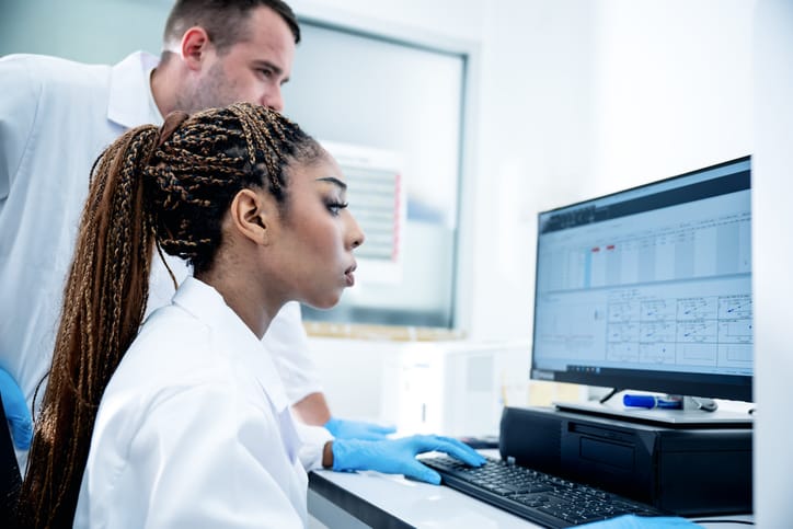 Photo shows two scientists using a computer to study results in a medical laboratory/Getty Images