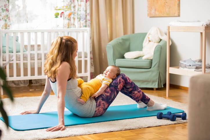 Photo shows a young mother working out at home on a mat with her baby/Getty Images