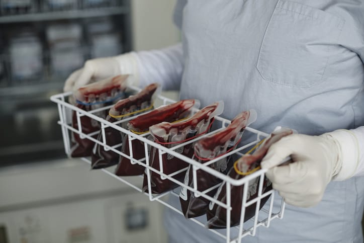 Photo shows the hands of a healthcare worker holding a rack of blood bags (Getty Images/Westend61)