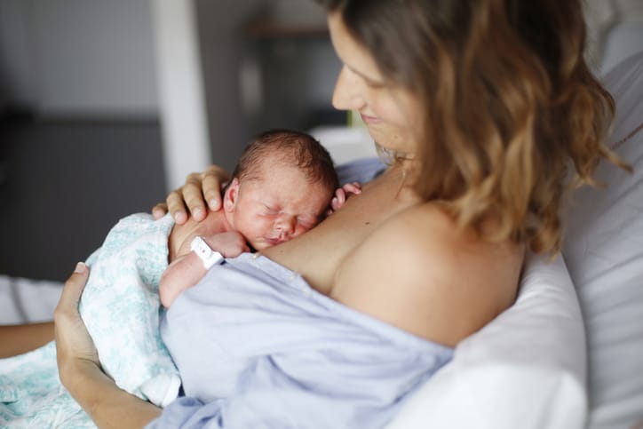 Photo shows a mother holding her newborn baby in a hospital bed/Getty Images