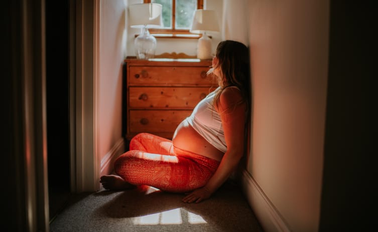Photo shows a pregnant woman sitting on the floor of her home/Getty Images/Catherine Falls Commercial