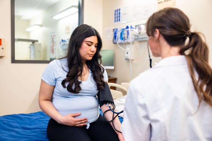 Photo shows a doctor and pregnant patient at a prenatal appointment in an exam room/Getty Images/adamkaz