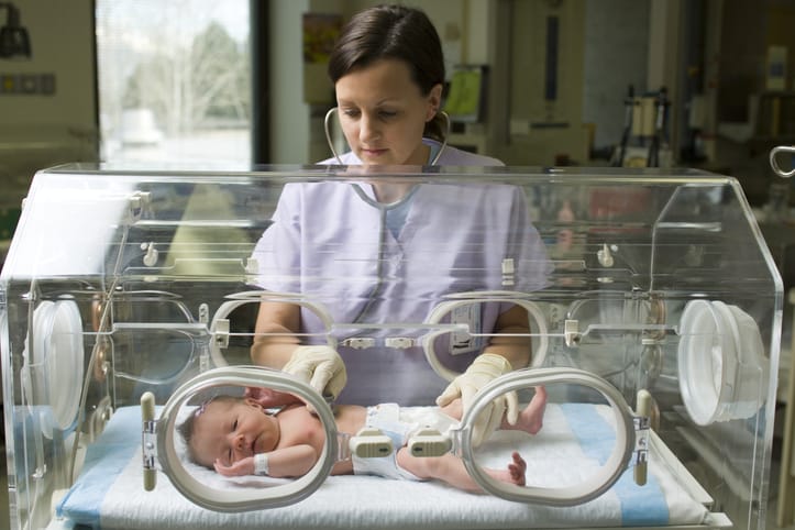 Photo shows a female nurse examining a newborn baby in an incubator/Getty Images/rubberball