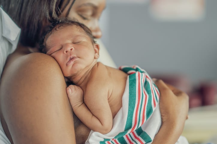 Photo shows a mother holding her baby on her shoulder as she sits up in her hospital bed and they spend time bonding skin-to-skin (Getty Images/FatCamera)